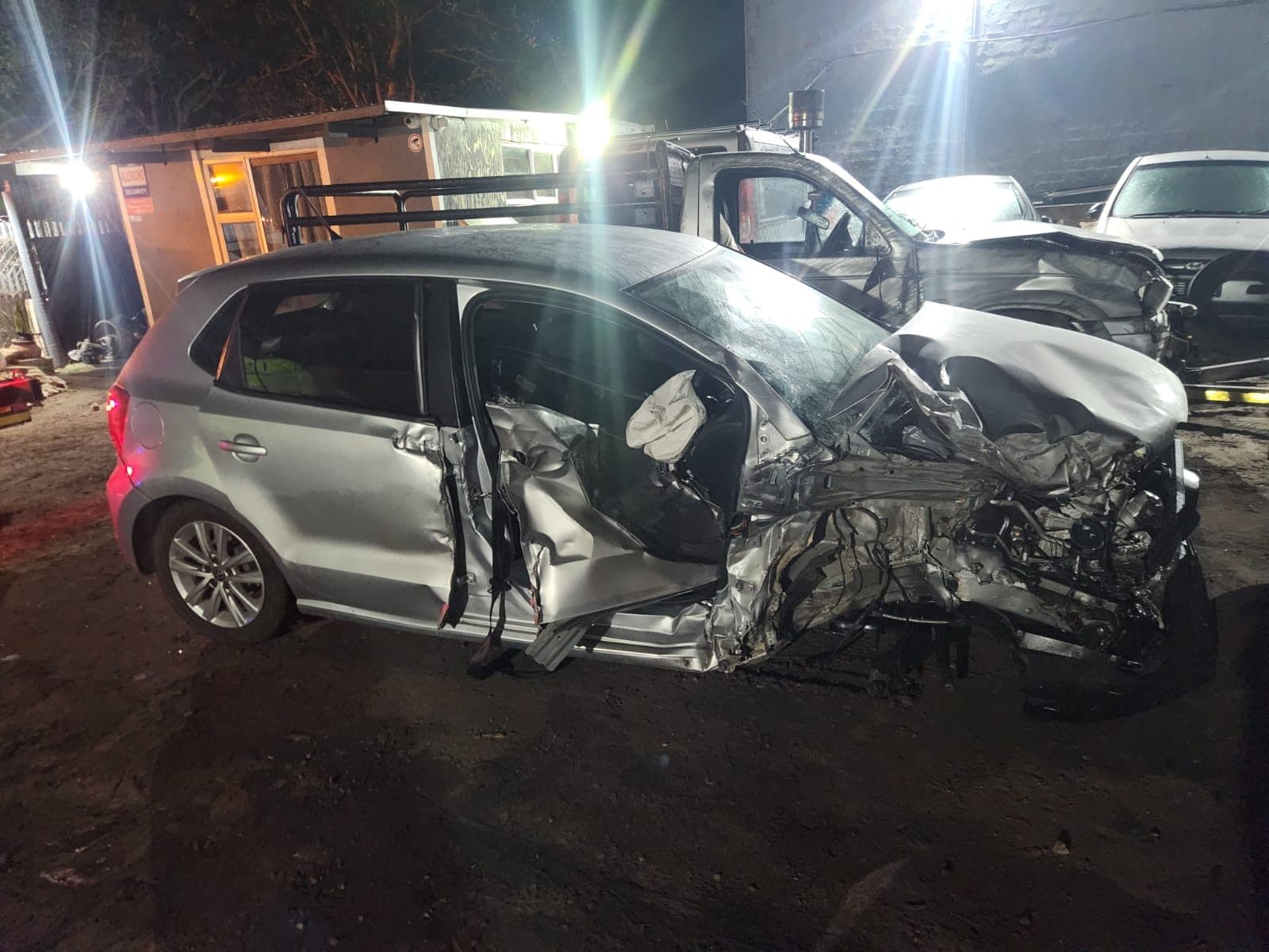 Side view of a silver VW Polo with its front end crushed and the driver's door pushed in